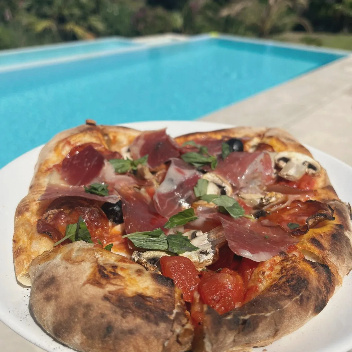 Wood-fired pizza with ham, served by the pool